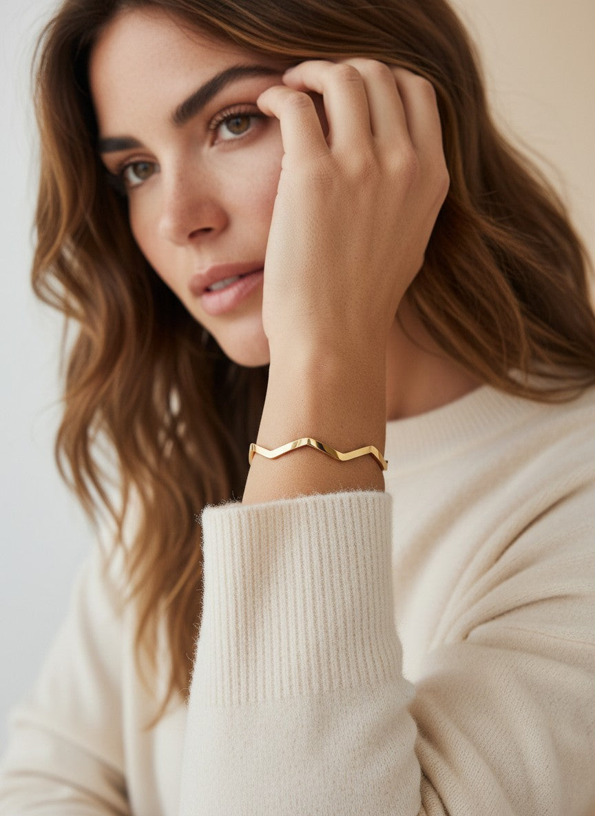 Daga-accessories rose gold-toned geometric wave bangle worn by a woman in a cream sweater