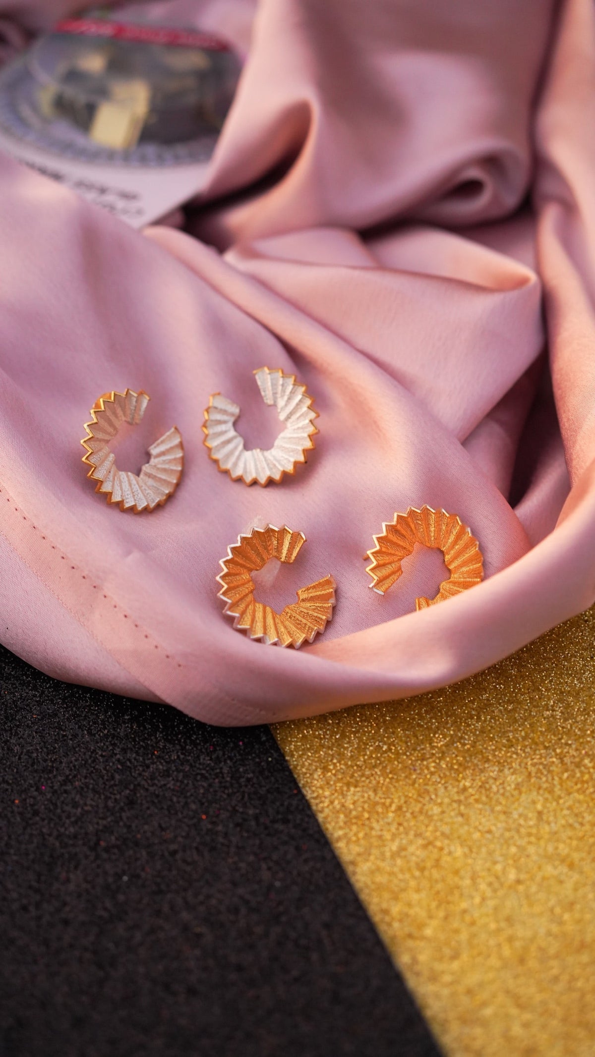 Daga-accessories The Classic Shaved Hoop earrings in gold and silver, displayed on soft pink silk fabric.
