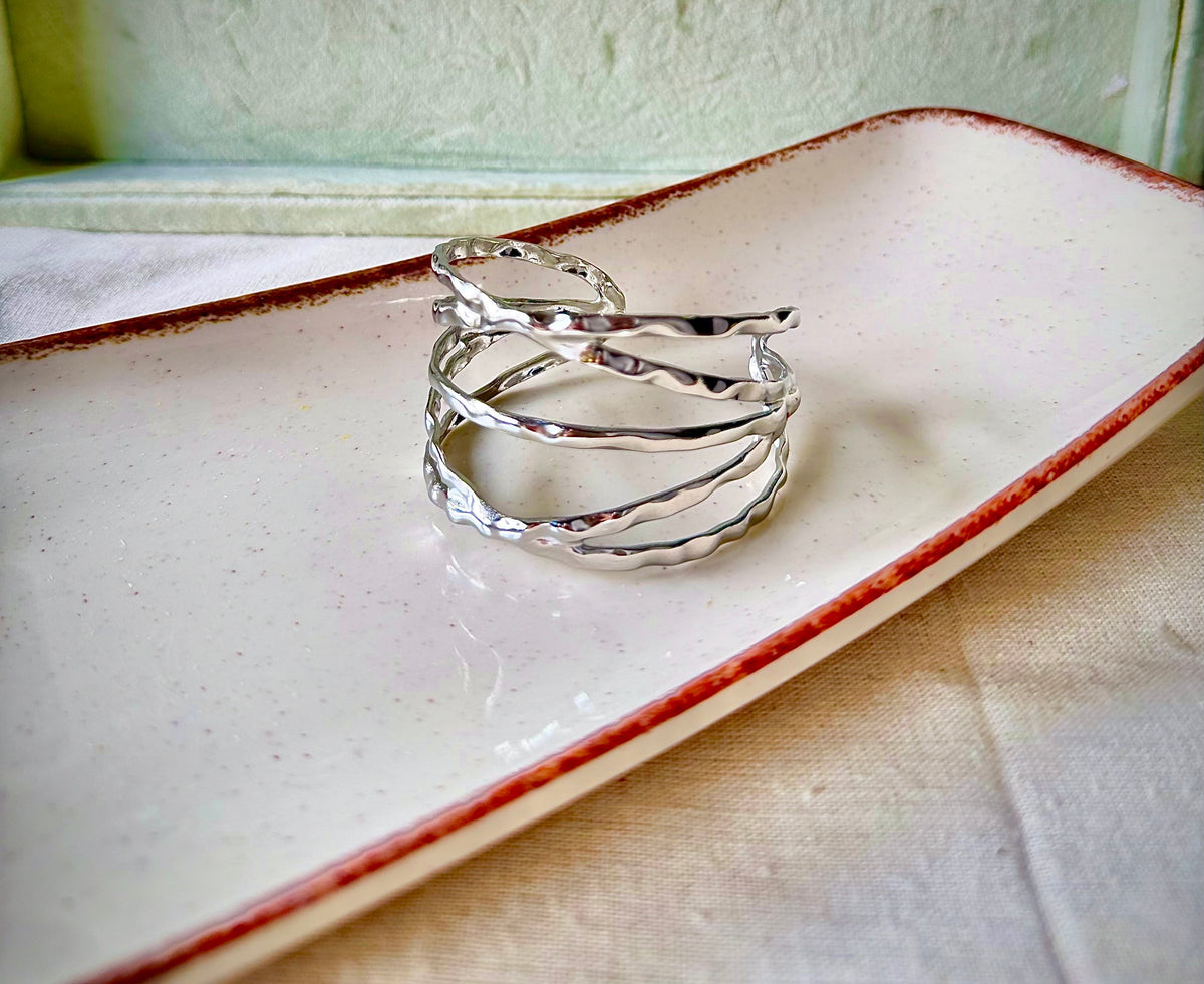 Daga-accessories silver open cuff bracelet with a modern hammered criss-cross design on a ceramic tray