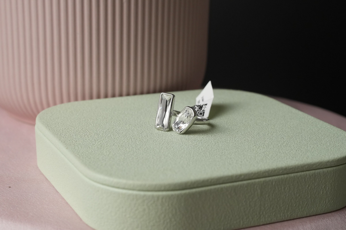 Daga-accessories silver-tone open ring with baguette and cushion cut crystals on a sage green display stand.