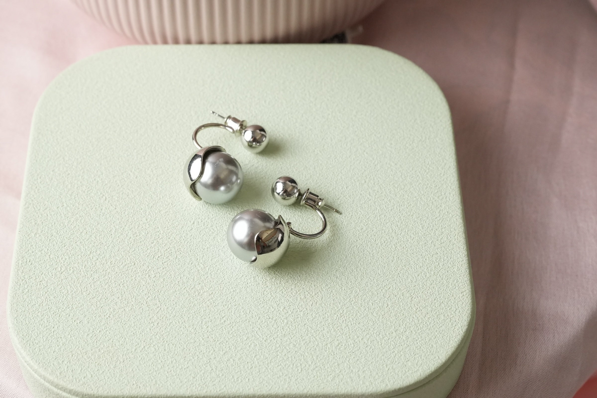 Daga-accessories silver-toned double-ball stud earrings with lustrous grey pearl-effect spheres on a green display