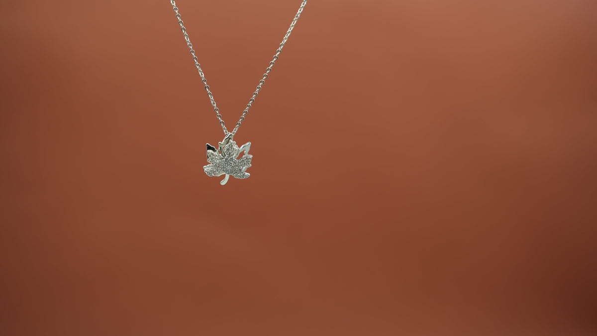 Daga-accessories silver maple leaf pendant necklace with intricate detailing on a delicate chain against a brown background