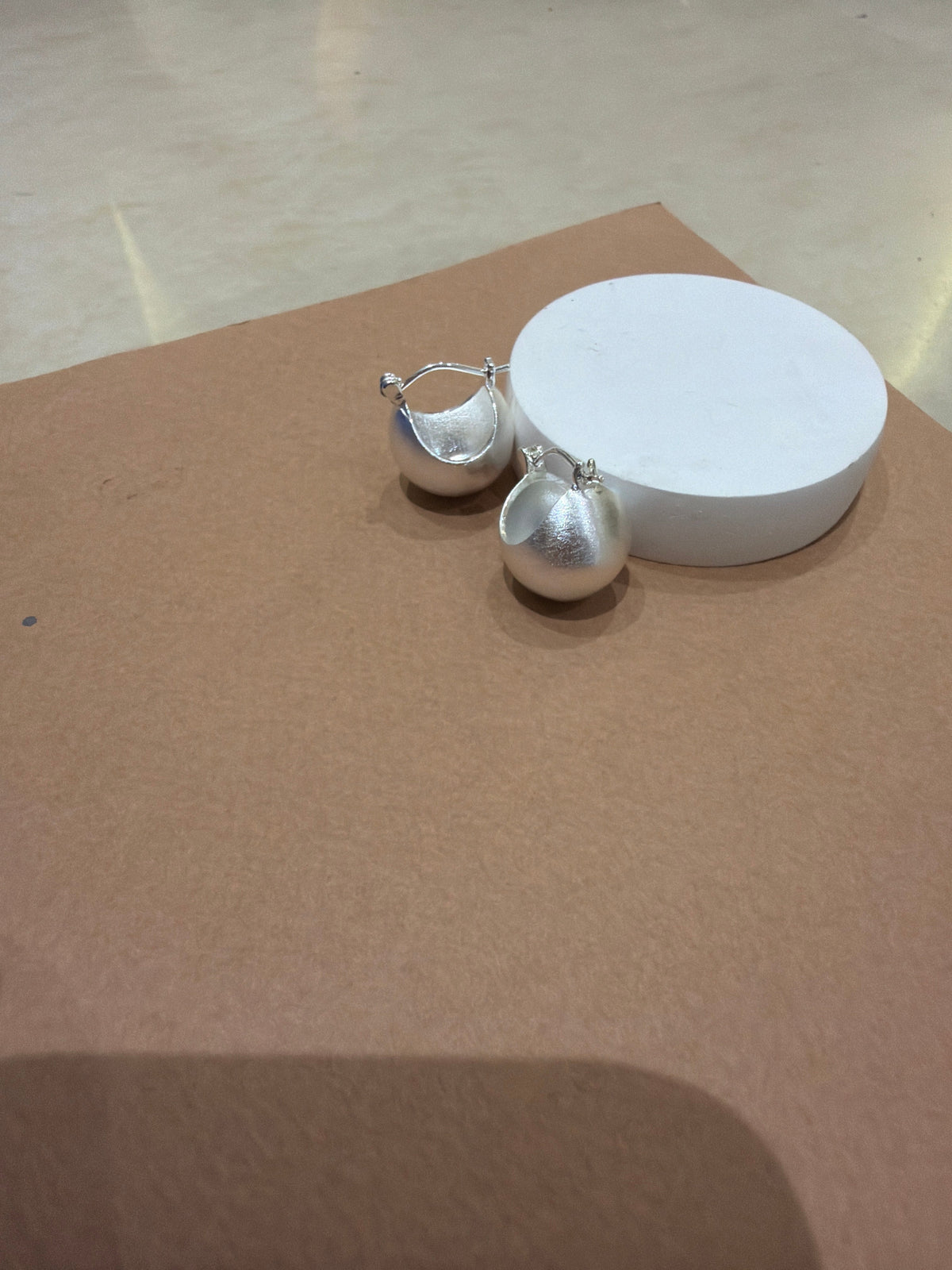 Daga-accessories silver Solar cup hoop earrings with a matte textured finish displayed on a white circular stand.