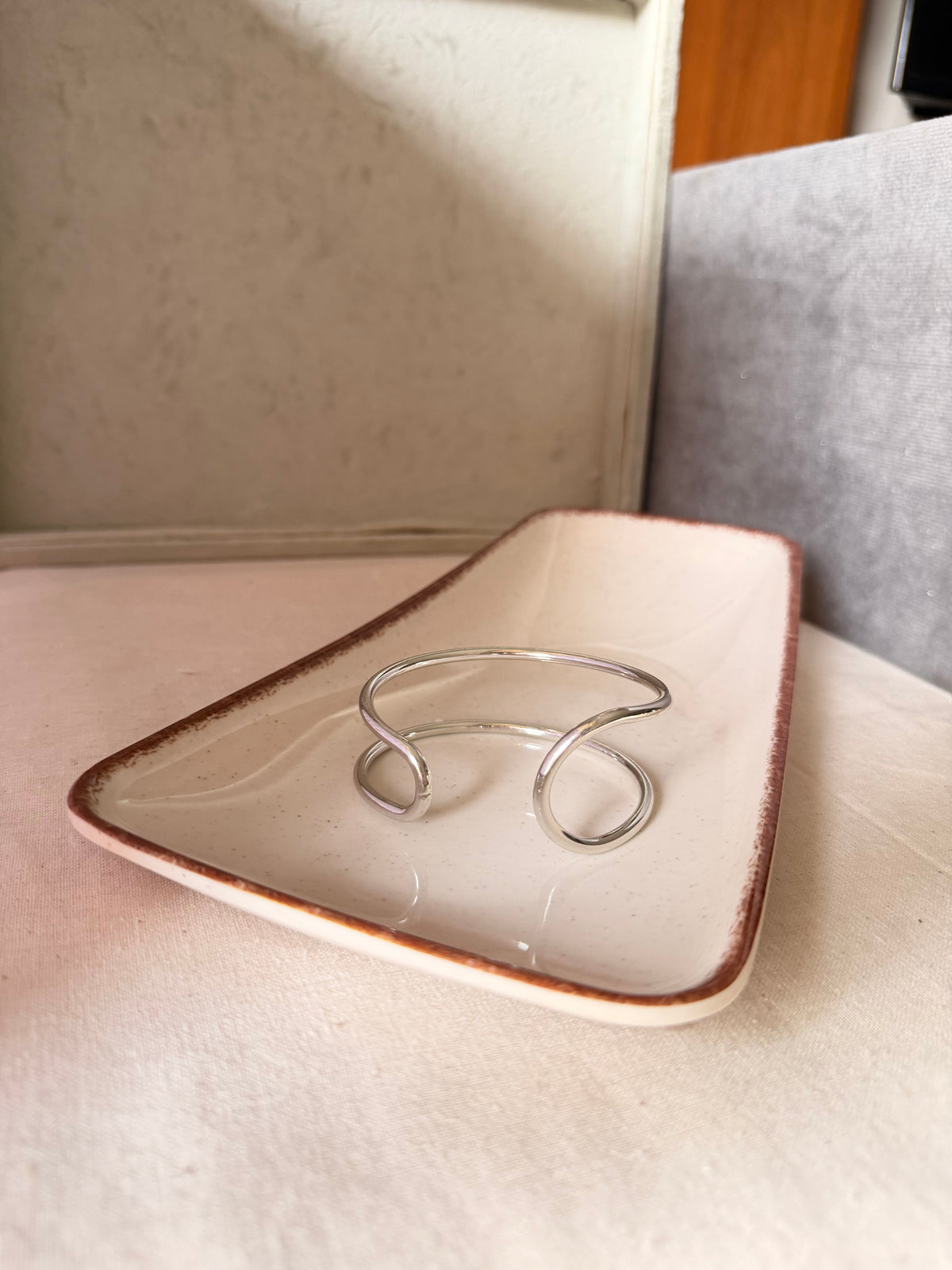 Daga-accessories minimalist silver open cuff bracelet with a fluid organic design resting on a ceramic tray