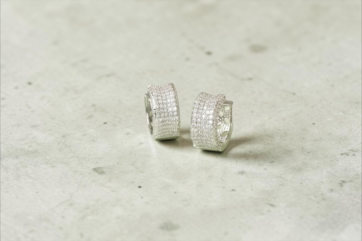 Daga-accessories silver-toned wide hoop earrings with pavé-style shimmering stones on a light green display stand