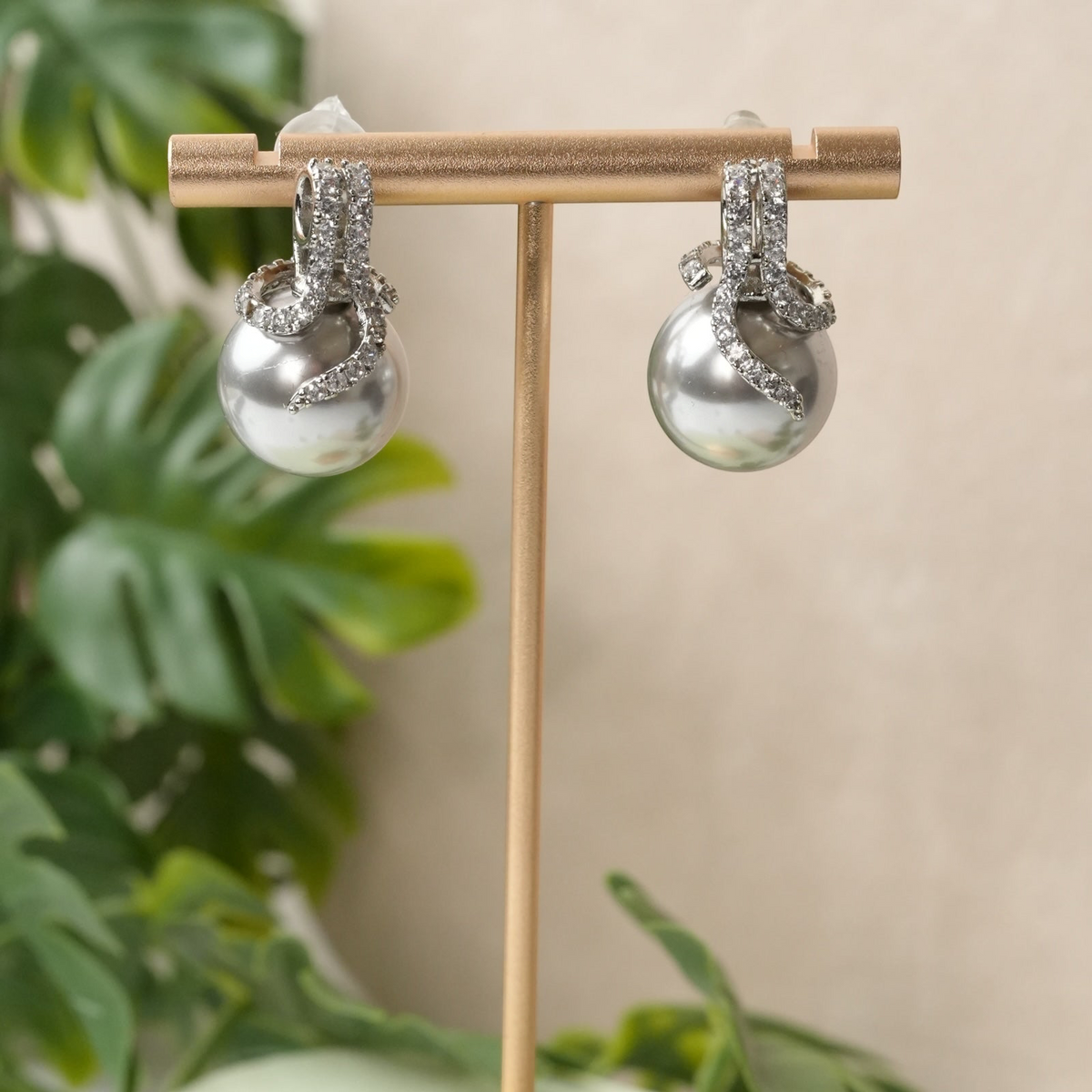 Daga-accessories silver-toned pearl drop earrings with cubic zirconia accents on a gold jewellery display stand.