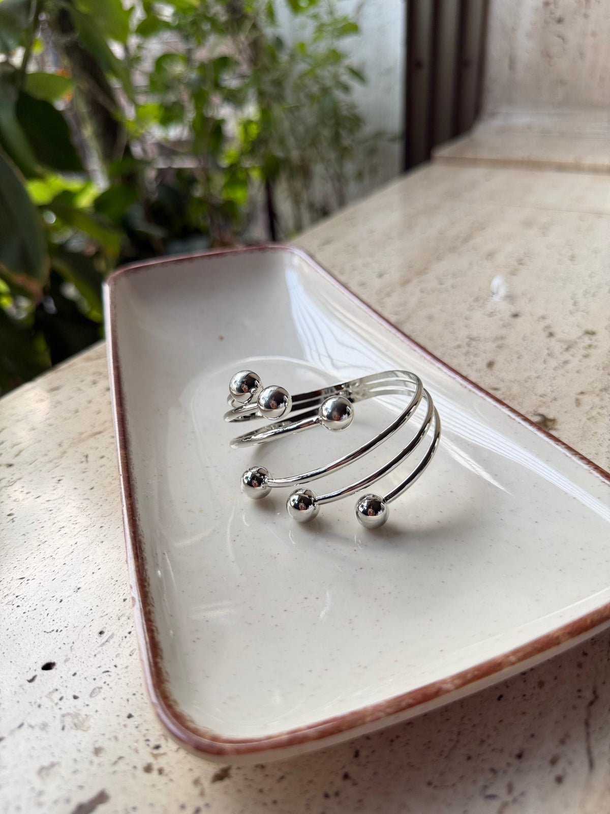 Daga-accessories silver spiral cuff bracelet with polished spherical terminals on a ceramic tray.