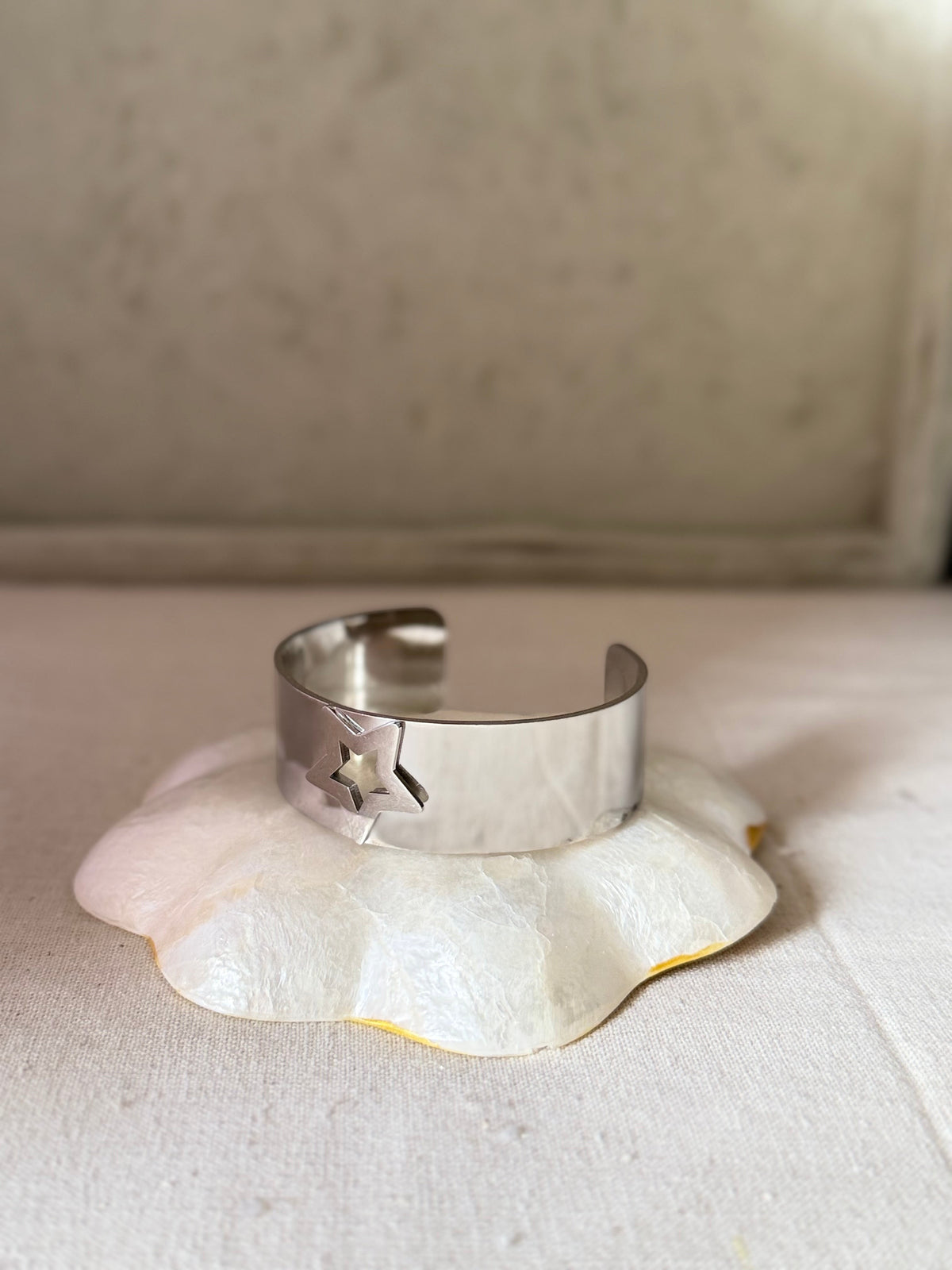 Daga-accessories silver cuff bracelet with star-shaped cut-outs on a white decorative base