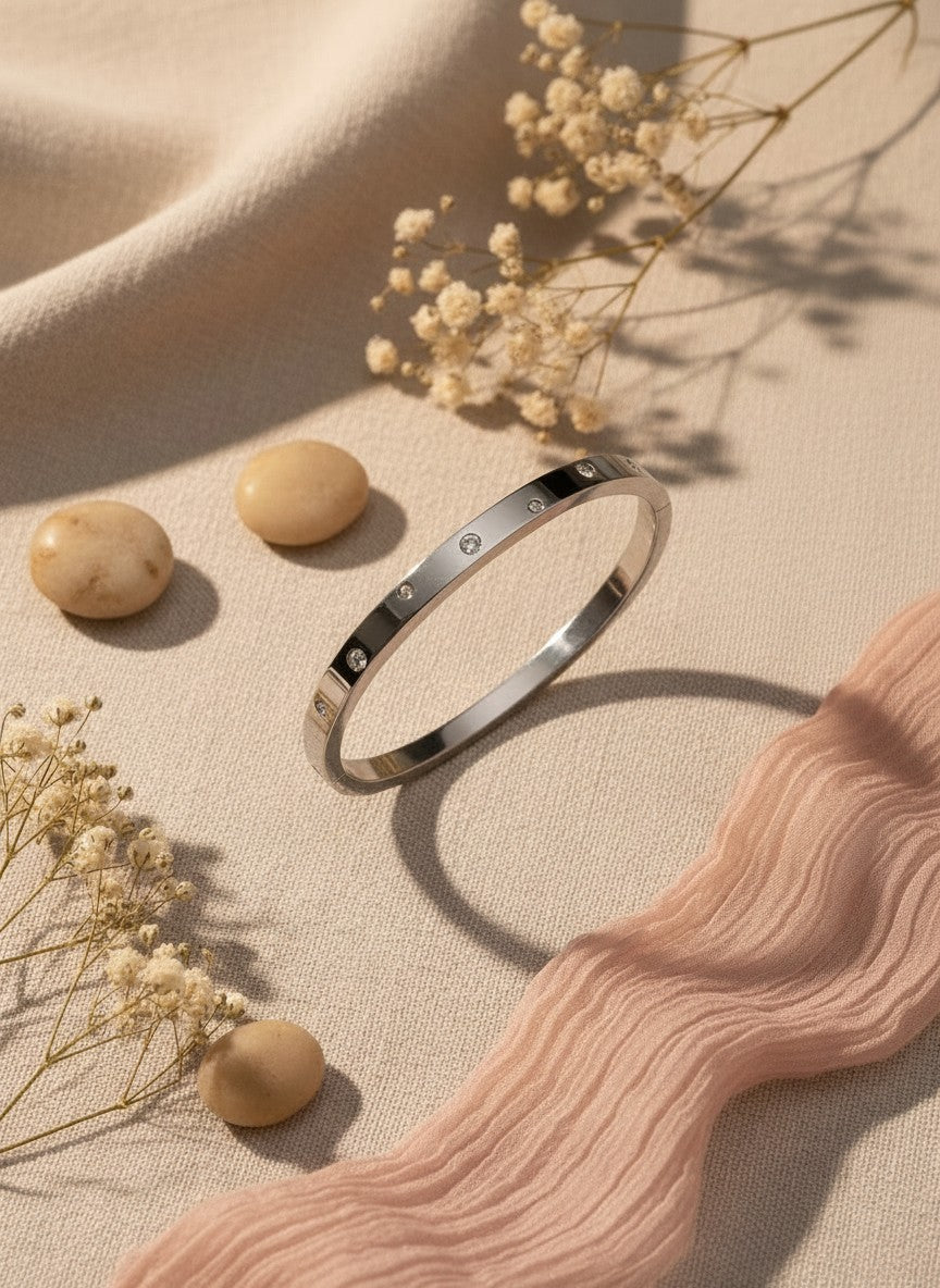 Daga-accessories silver stainless steel bangle with embedded stones on a beige fabric background with dried flowers.