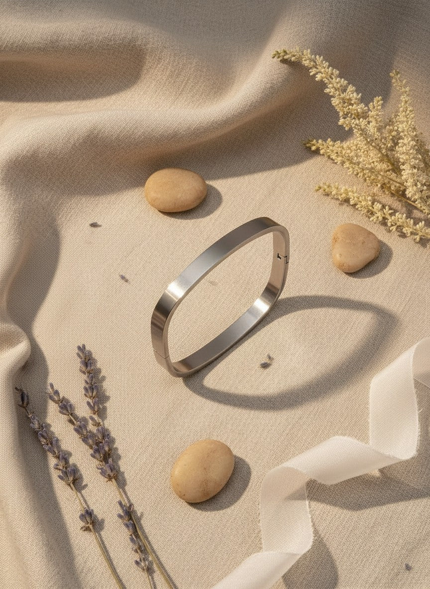 Daga-accessories minimalist square-oval stainless steel bangle bracelet with a polished finish on beige fabric.