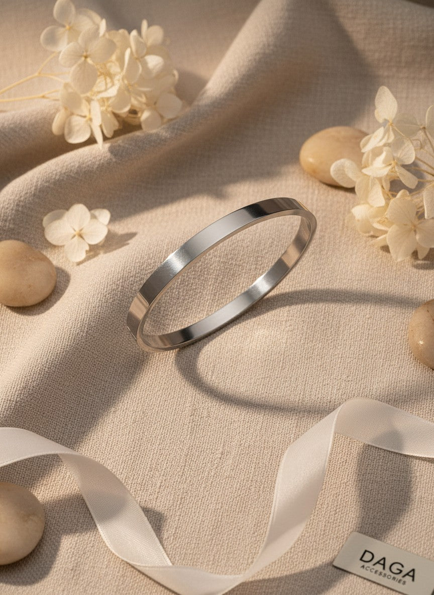 Daga-accessories minimalist stainless steel bangle with a brushed metallic finish on a beige fabric background.
