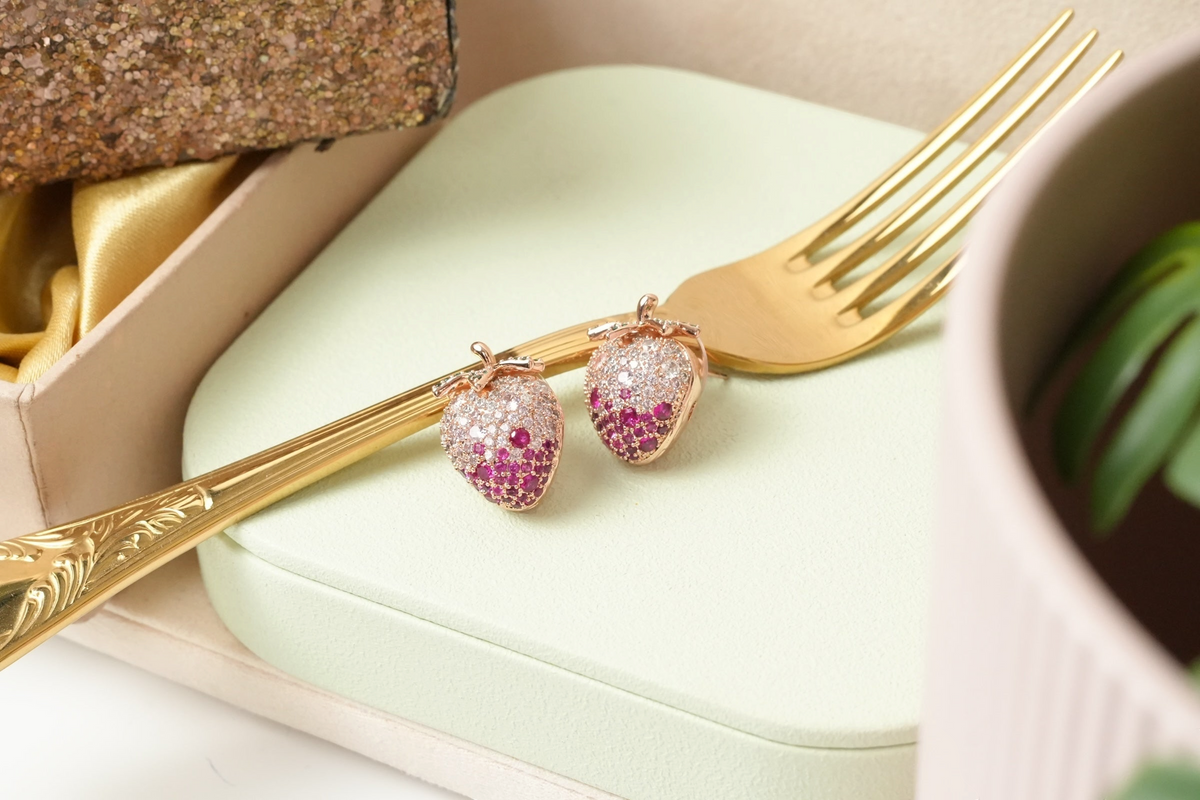 Daga-accessories strawberry stud earrings in rose gold with pink and clear cubic zirconia stones on a gold fork.