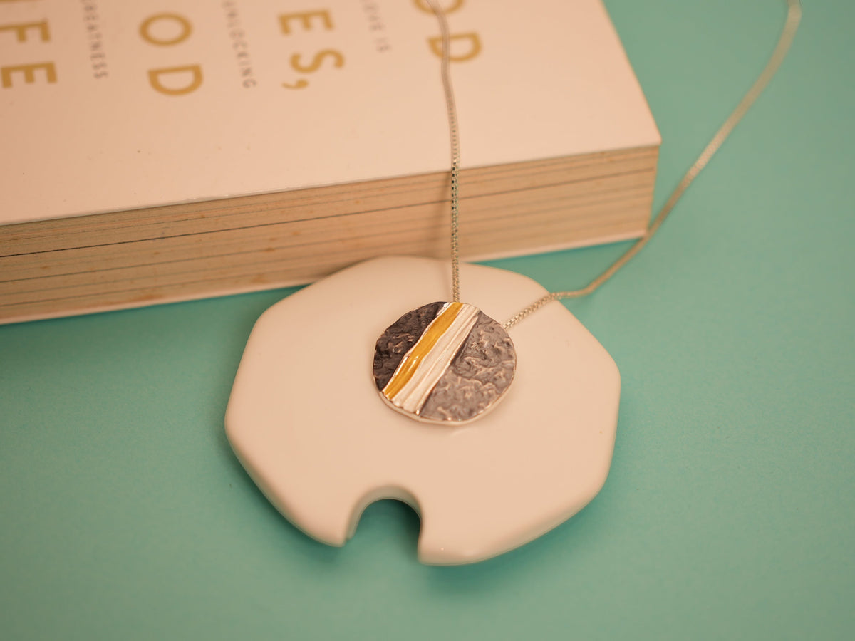 Daga-accessories textured circular pendant necklace with a hammered finish and polished gold stripe on a delicate chain