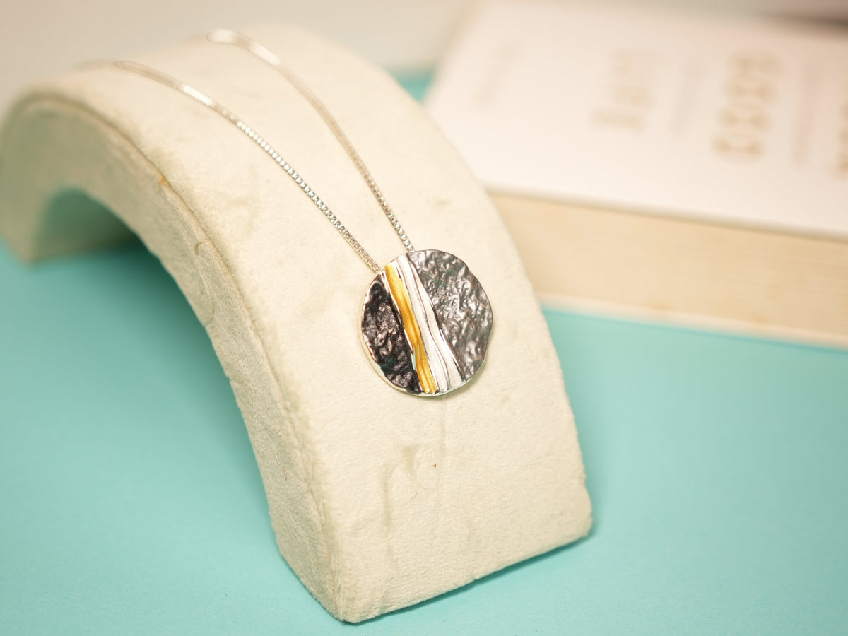 Daga-accessories textured circular pendant necklace with hammered silver and gold metallic stripe on a delicate chain