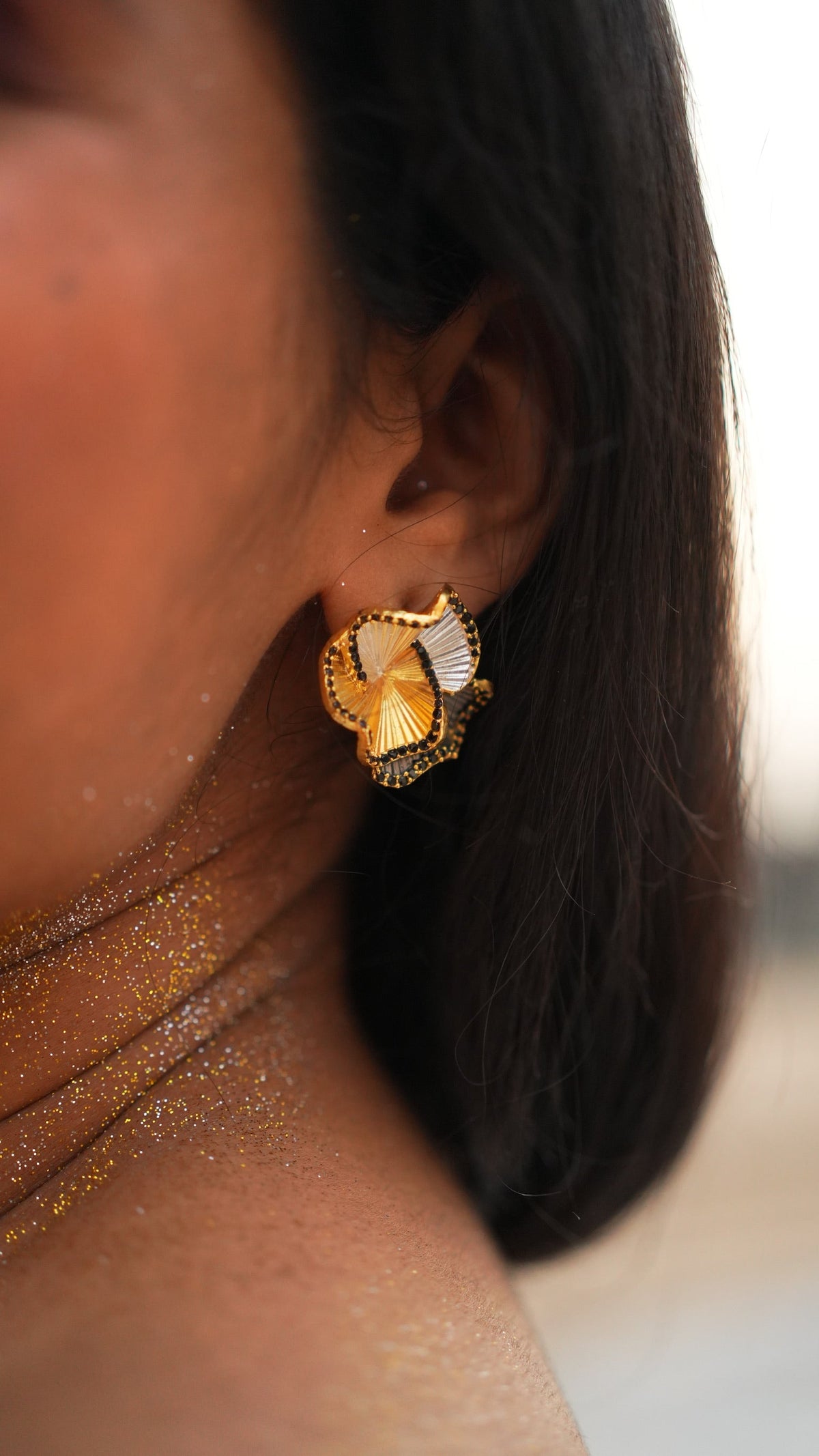 Daga-accessories Three Petal Elegance stud earring featuring gold, white, and black textured petals on a woman's ear.
