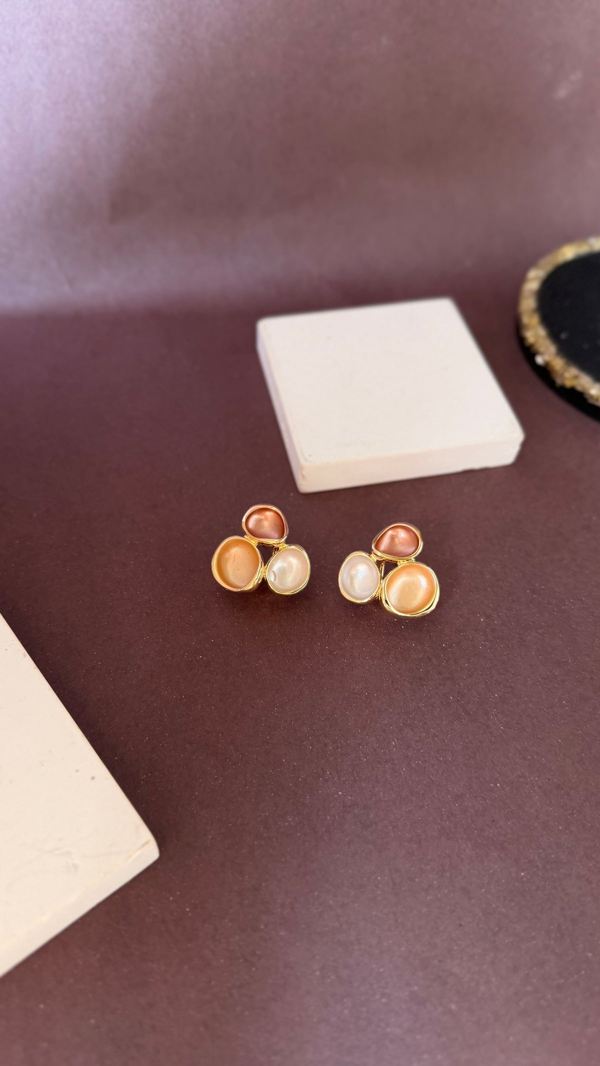 Daga-accessories Threefold bloom gold-toned earrings with mocha and cream swirl accents on a dark brown surface.