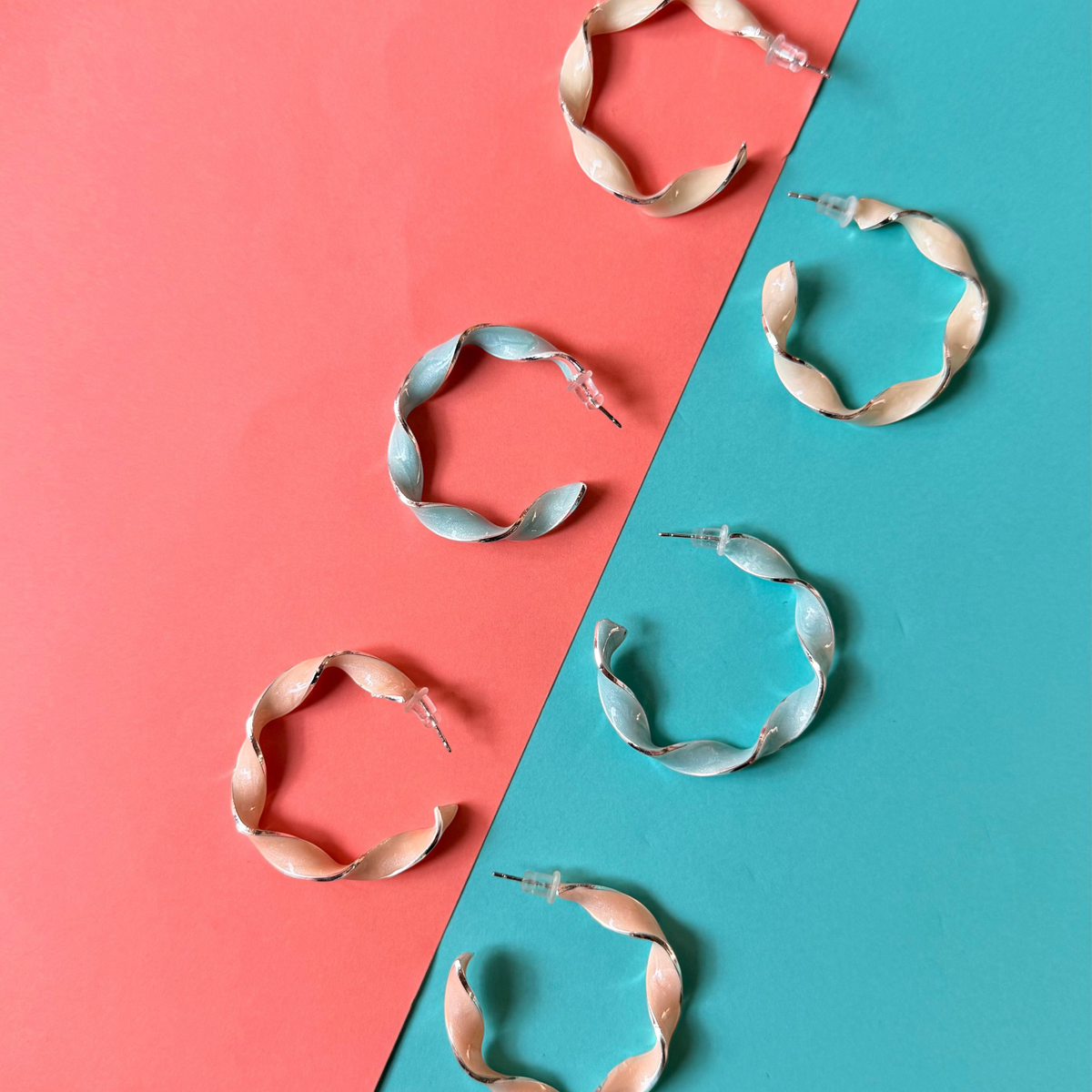 Daga-accessories Sky Fusilli hoop earrings in pastel blue and peach enamel with a twisted design on a colorful background