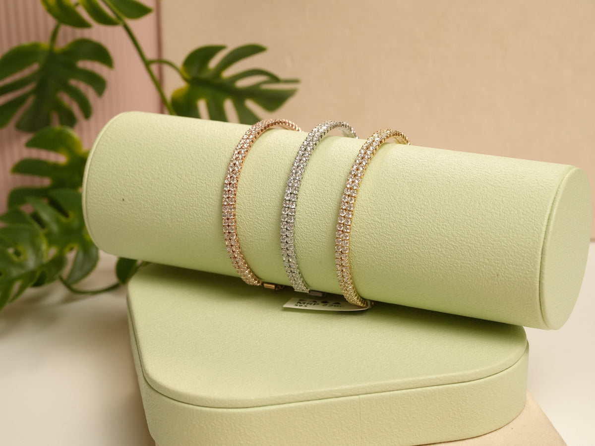 Daga-accessories rose gold, silver, and gold two-liner bracelets with studded detailing on a green display stand.