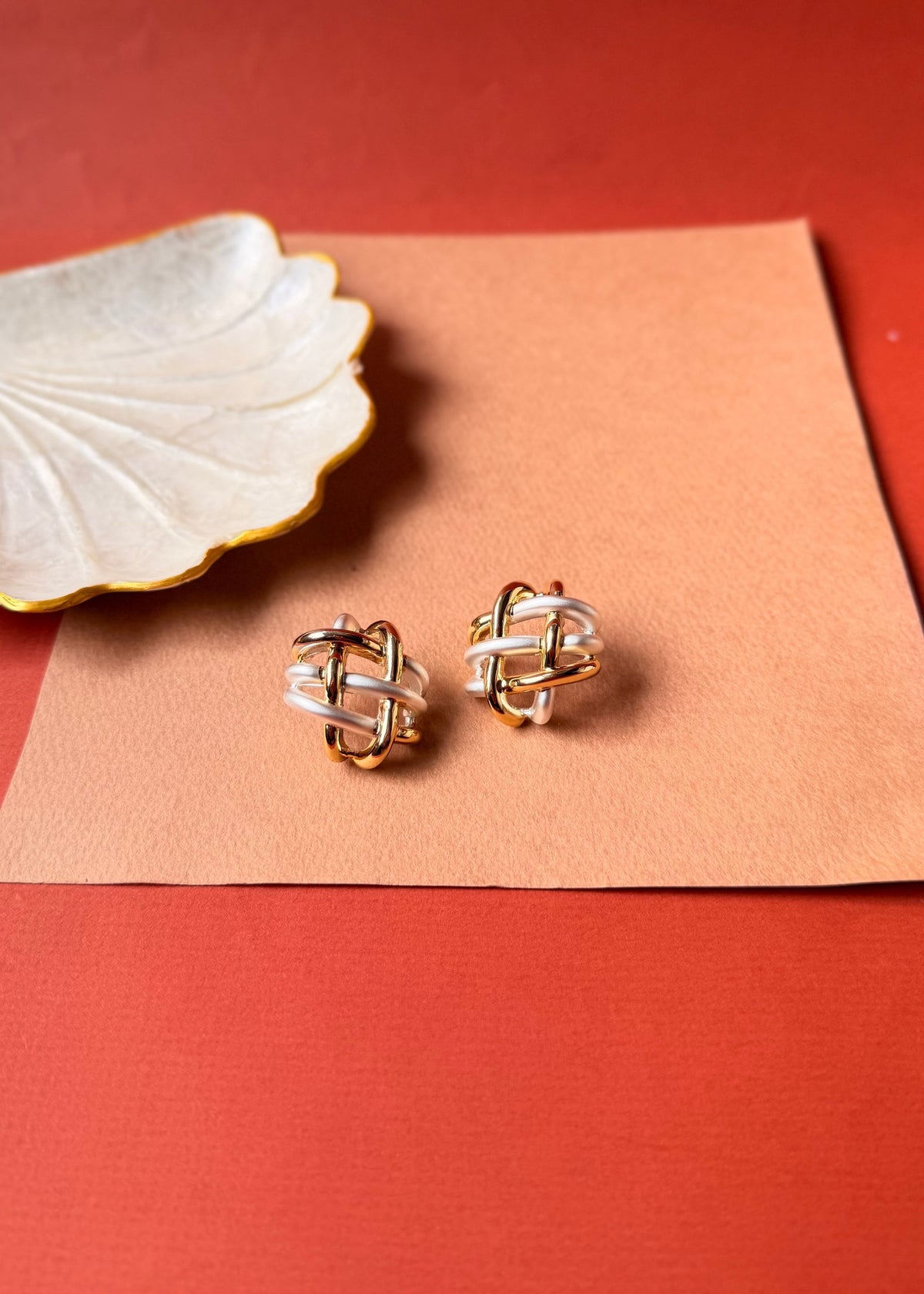 Daga-accessories Auric silver drift two-tone gold and silver knot stud earrings on a textured paper background.