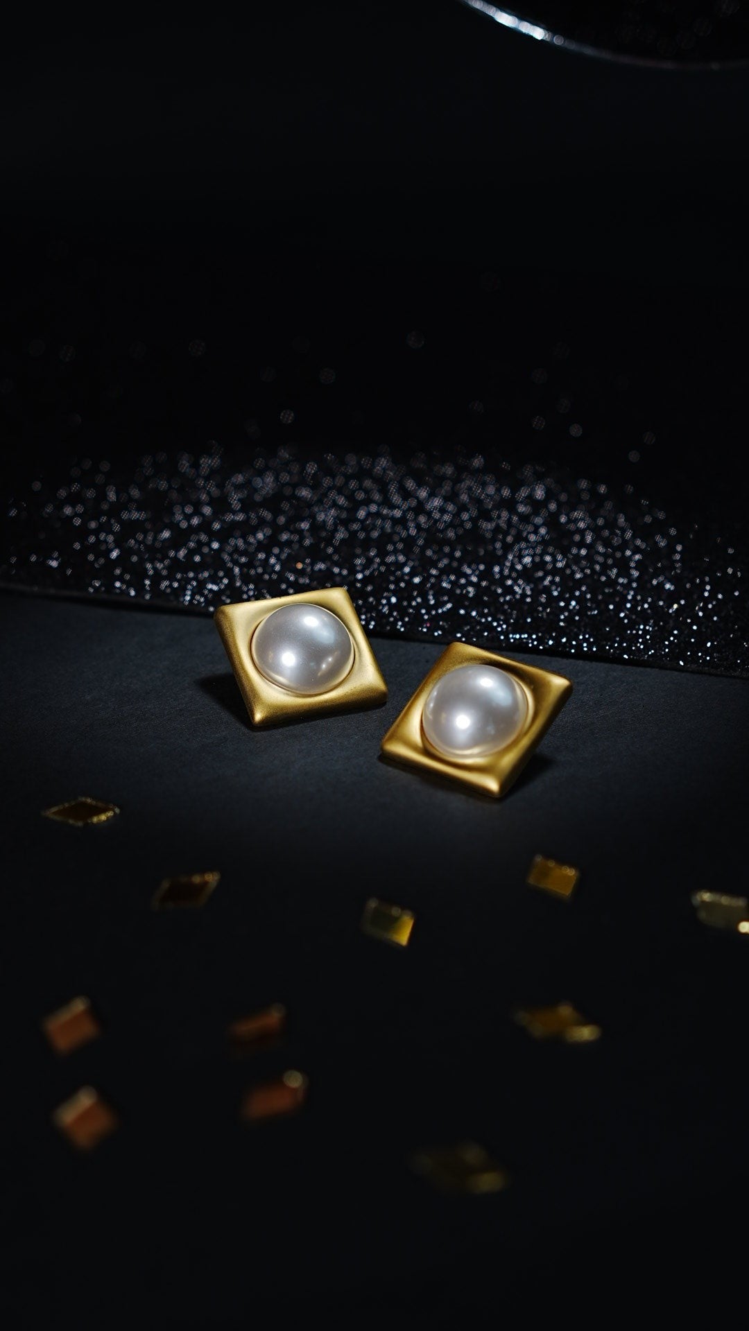 Daga-accessories vintage square stud earrings in antique gold with a central pearl, set against a black background.