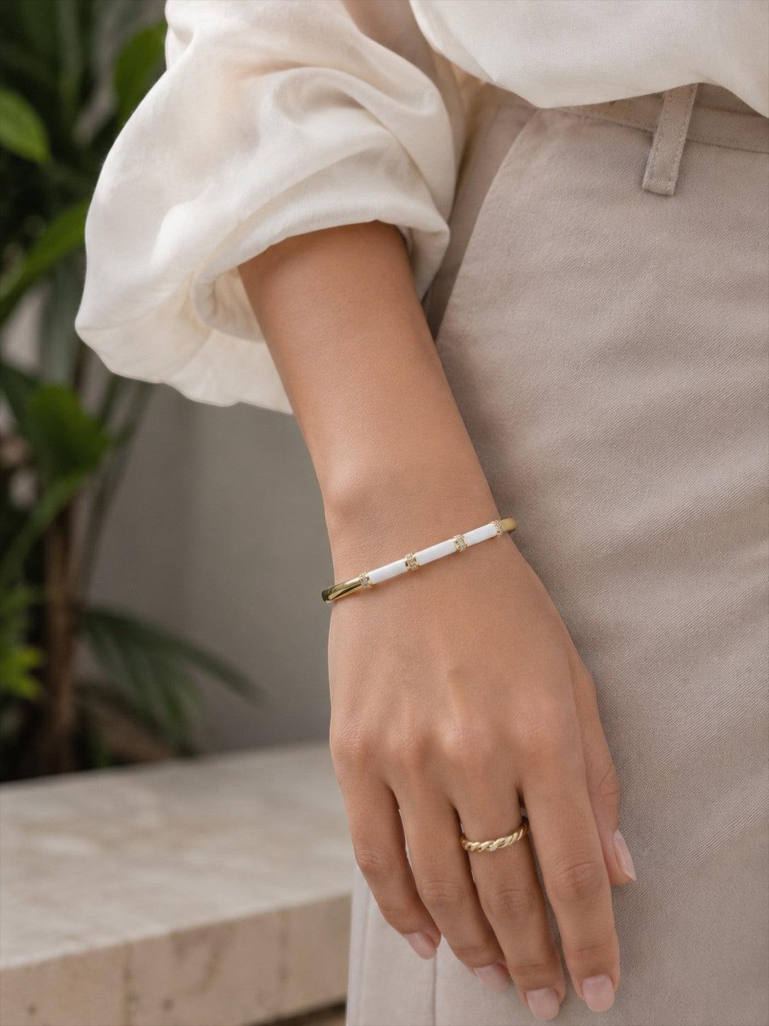 Daga-accessories white enamel bar bracelet with gold accents worn on a wrist with a matching gold ring