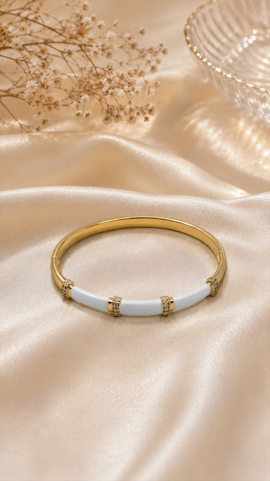 Daga-accessories white enamel and gold bar bracelet with sparkling crystal accents on a soft champagne silk fabric