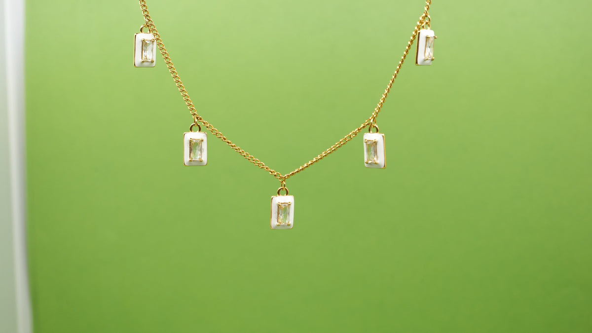 Daga-accessories white enamel and gold stainless steel necklace with rectangular studded charms against green background